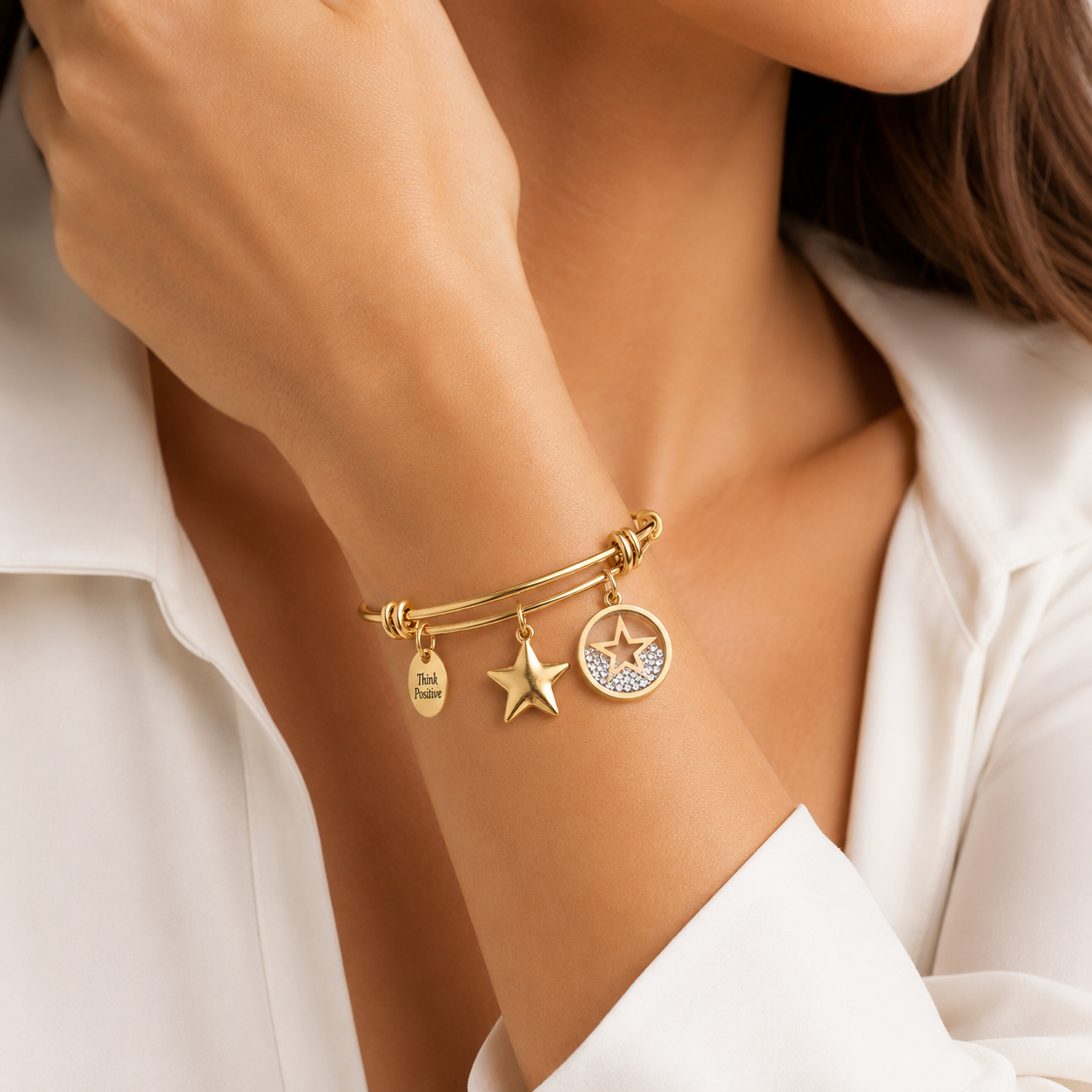 bratara rigida think positive din otel inoxidabil 316 L hipoalergenic placat cu rodiu auriu cu charmsuri stele cu cristale swarovski la mana unui model feminin elegant