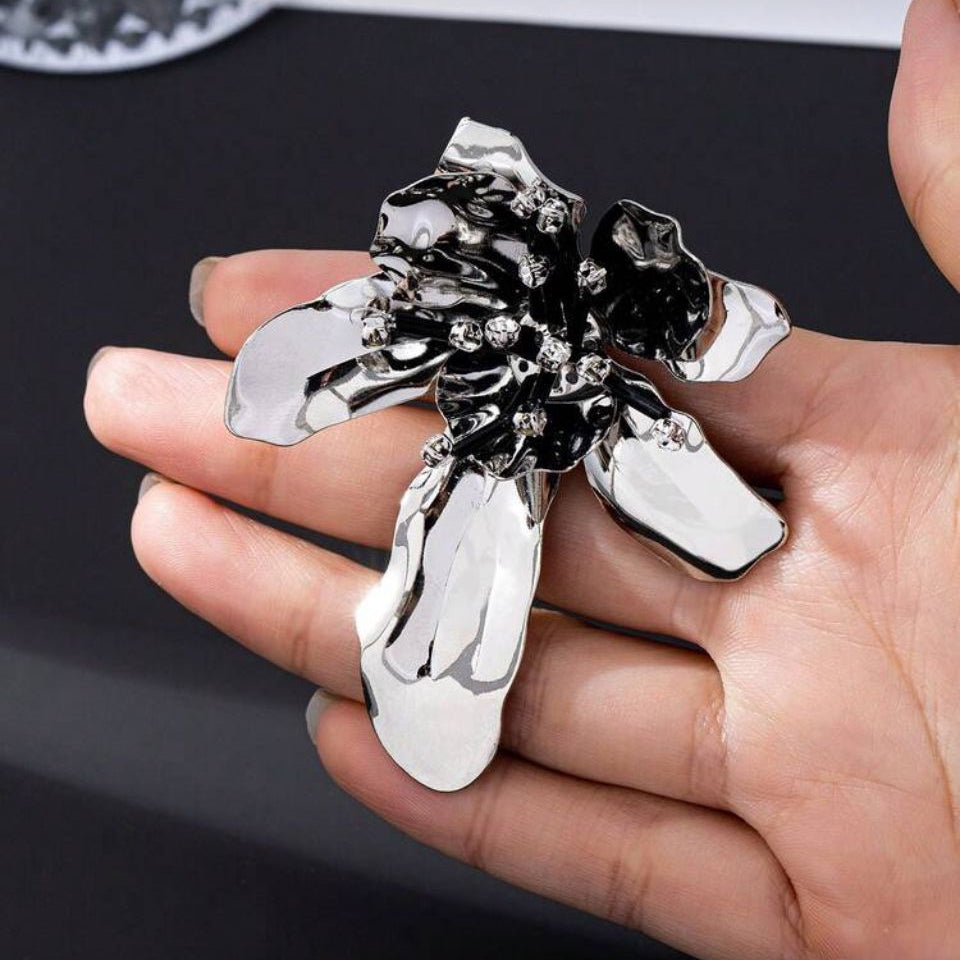 Brosa mare din metal argintiu in forma de floare sculpturala cu petale lucioase, pistil negru si cristale albe tinuta in mana