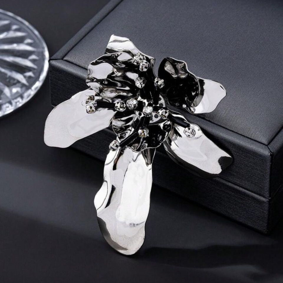 Brosa mare din metal argintiu in forma de floare sculpturala cu petale lucioase, pistil negru si cristale albe