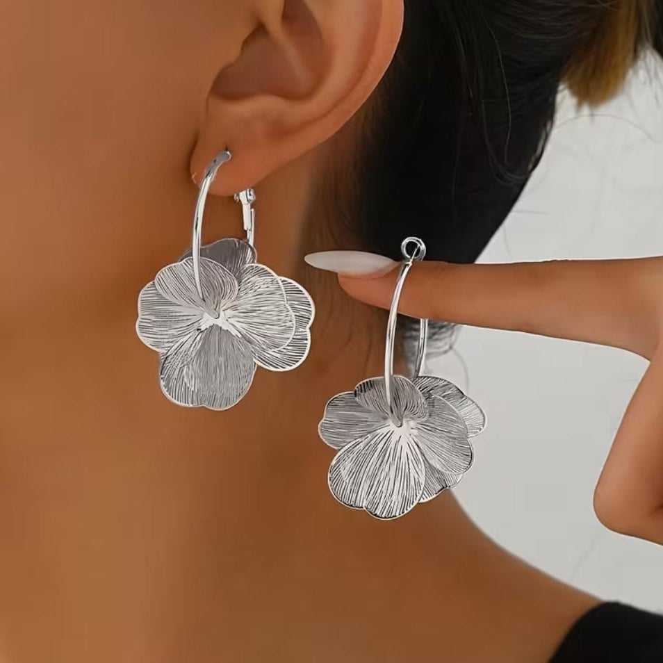 Model feminin purtand cerceii mari de tip tortita cu floare argintie, evidentiind proportiile statement de 5.2 cm si asezarea eleganta pe lob