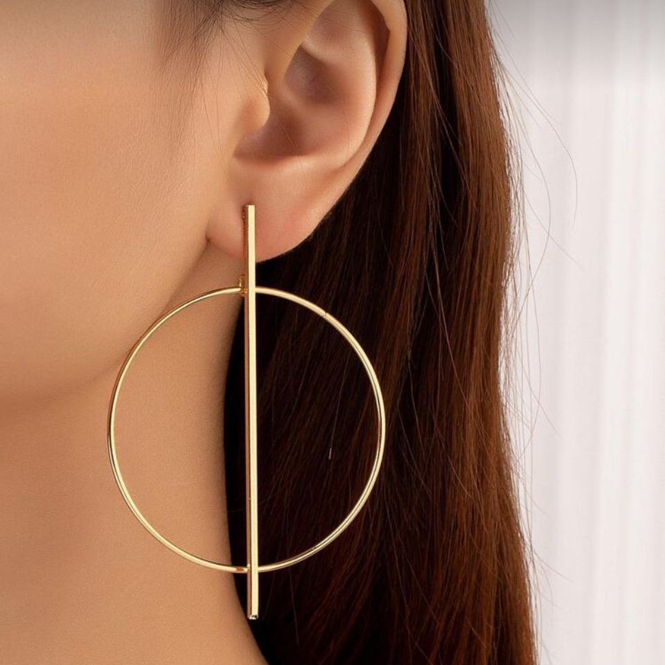 Cercei statement aurii mari cu design geometric format dintr-un cerc intretaiat de o bara verticala, stil minimalist modern Lasardo Gioielli la ureche