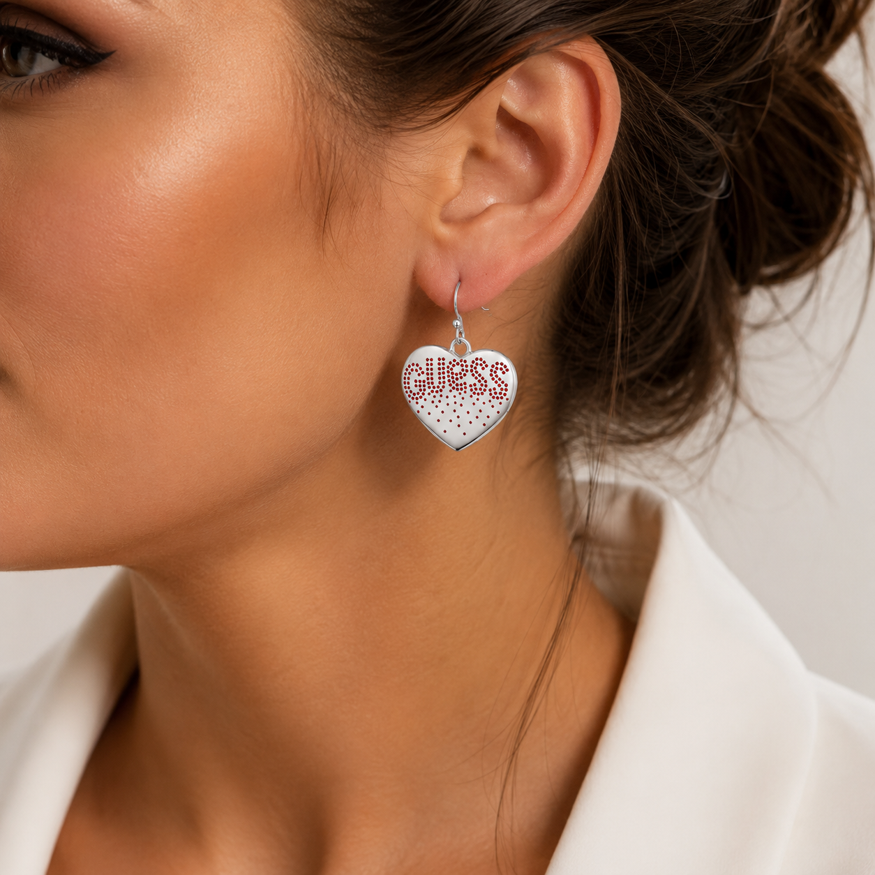 Model feminin purtand cerceii inima Guess statement de 30 mm din otel chirurgical cu tortita evidentiind volumul si proportiile bijuteriei.