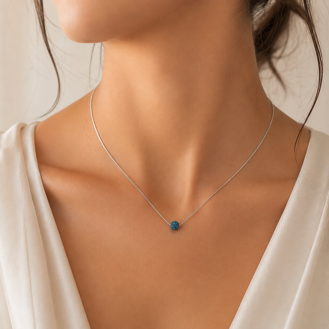Detaliu la baza gatului cu un model feminin purtand colierul subtire din argint cu pandantiv sferic din cristale swarovski albastre.