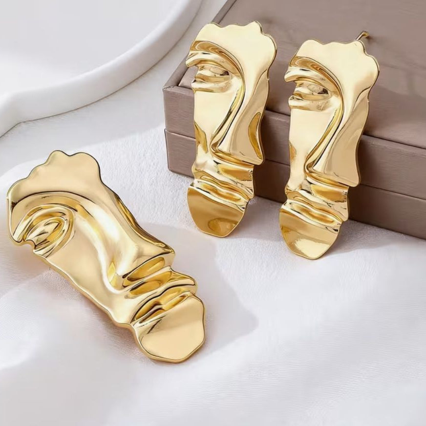 Set premium de dama din metal placat auriu compus din cercei si brosa in forma de masca abstracta suprarealista pe fundal elegant