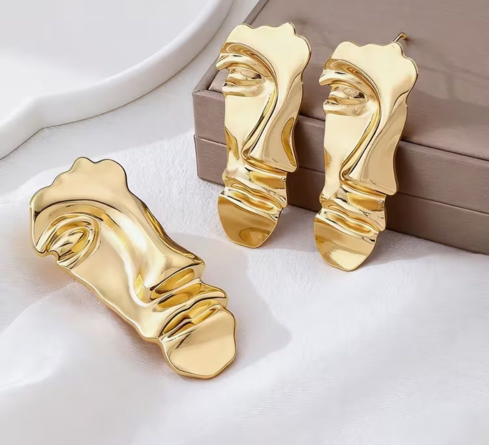 Set premium de dama din metal placat auriu compus din cercei si brosa in forma de masca abstracta suprarealista pe fundal elegant