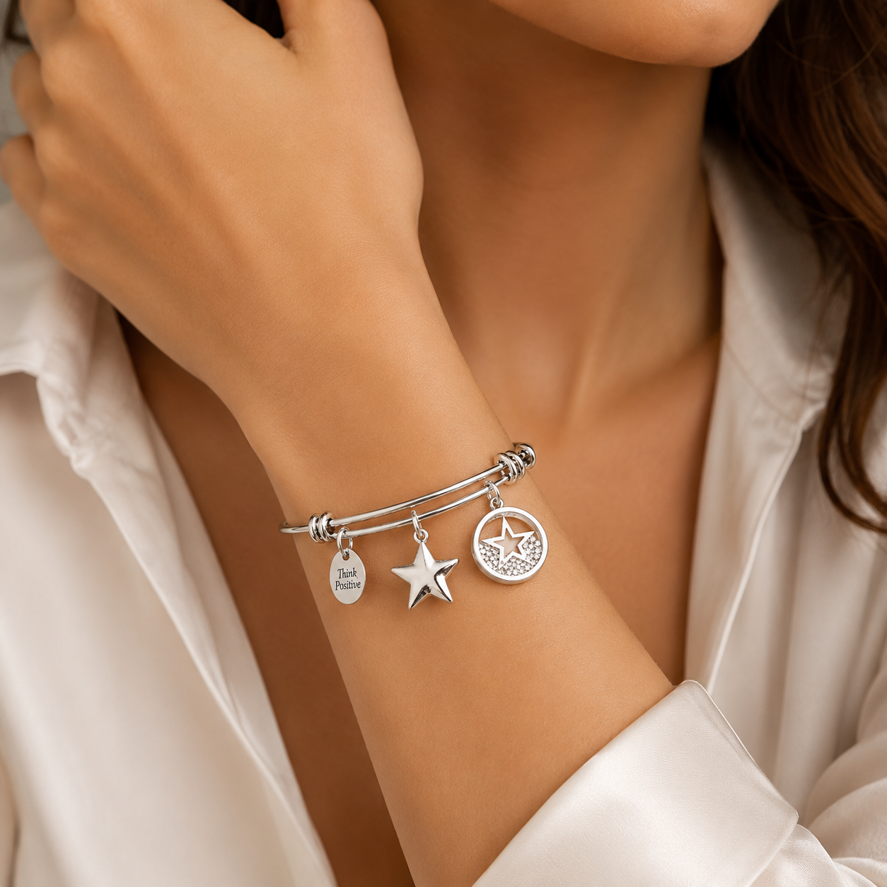 bratara rigida think positive din otel inoxidabil 316 L hipoalergenic placat cu rodiu cu charmsuri stele cu cristala swarovski la mana unui model feminin elegant