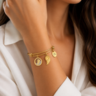bratara rigida think positive din otel inoxidabil 316 L hipoalergenic auriu cu charmsuri aripa de inger si cristale swarovski la mana unui model feminin elegant
