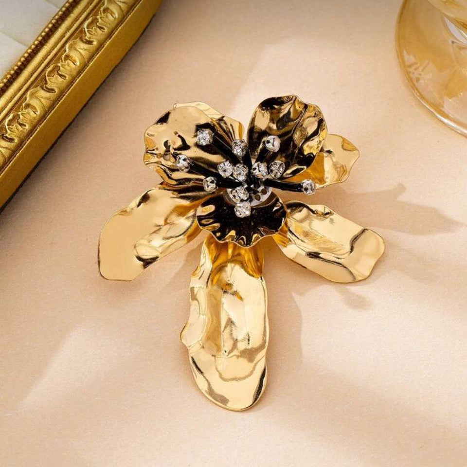 Brosa mare din metal auriu in forma de floare sculpturala cu petale lucioase, pistil negru si cristale albe