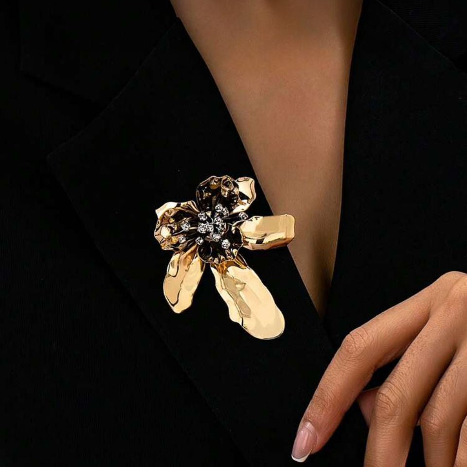 Model feminin purtand brosa mare in forma de floare aurie pe reverul unui sacou, punand in valoare proportiile statement de 7 cm si asezarea spectaculoasa