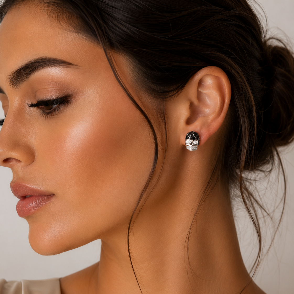   Pereche de cercei din argint 925 in forma de craniu sculptural, decorati cu un pavaj de cristale negre pe crestet si diamante cz albe pentru ochi si dinti, pusi la urechea unui model feminin