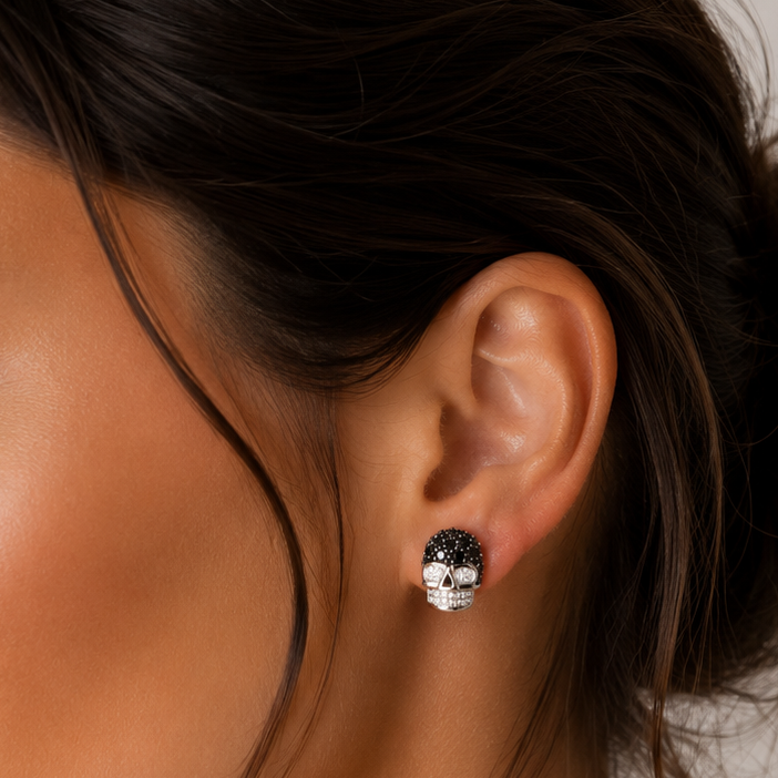 close up pereche de cercei din argint 925 in forma de craniu sculptural, decorati cu un pavaj de cristale negre pe crestet si diamante cz albe pentru ochi si dinti, pusi la urechea unui model feminin