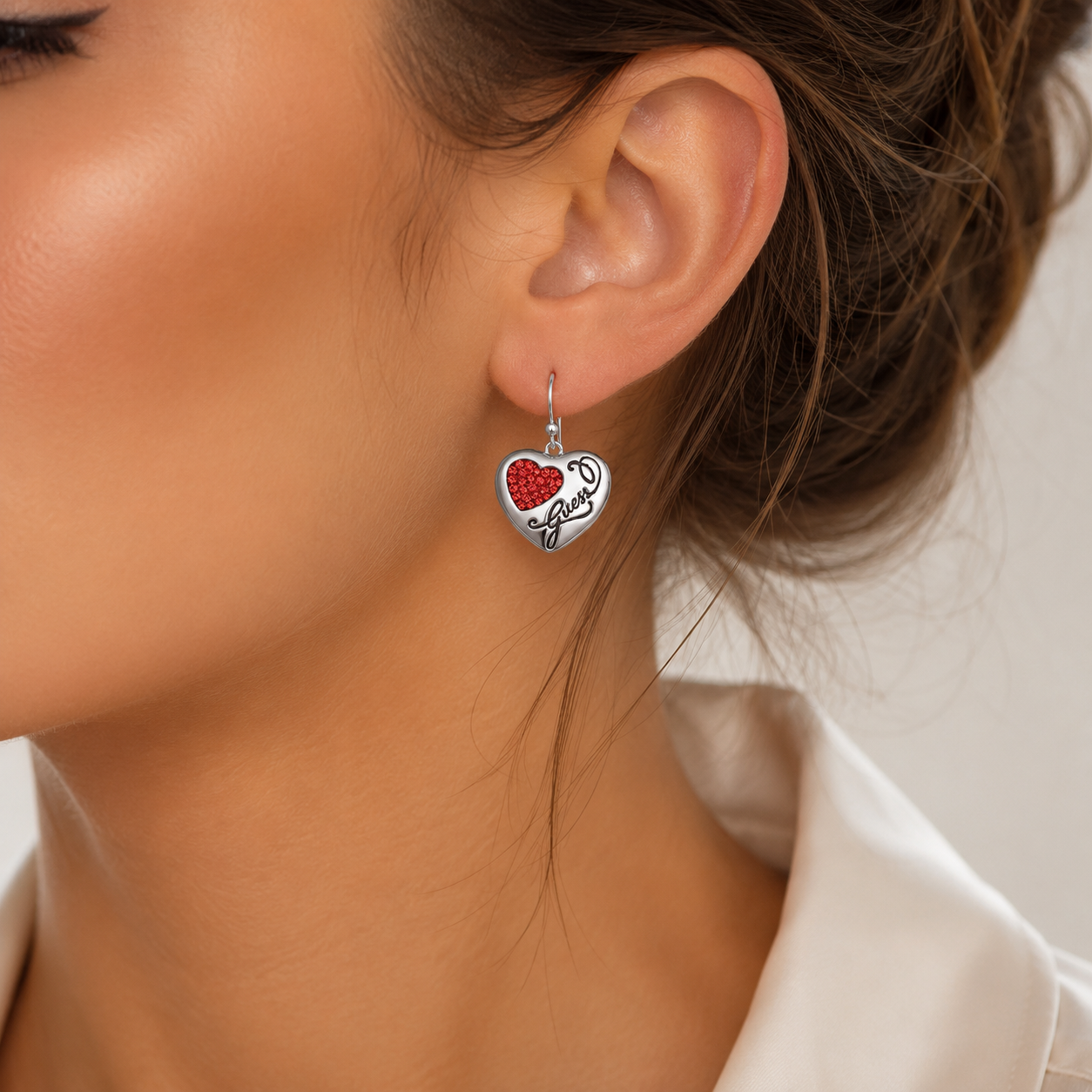 Detaliu cu un model feminin purtand cerceii Guess suspendati pe tortita evidentiind lungimea de 2,5 cm si reflexiile intense ale cristalelor swarovski rosii