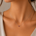 Model feminin purtand colierul fin din argint rodiat cu pandantiv rotund din cristale swarovski mov la baza gatului.