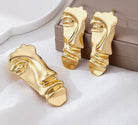 Set premium de dama din metal placat auriu compus din cercei si brosa in forma de masca abstracta suprarealista pe fundal elegant